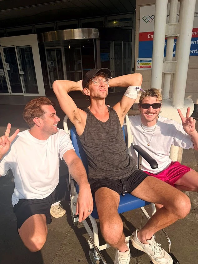 Ross sitting outside a hospital between two other people, all smiling